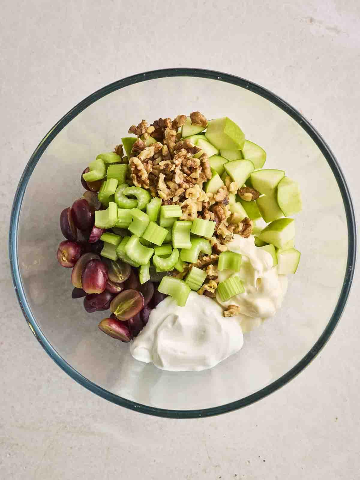 Gli ingredienti tritati per un'Insalata Waldorf in una ciotola di vetro, pronti per essere mescolati, per il passo 2 della ricetta.