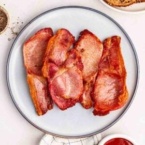 Bacon Perfetto nella Friggitrice ad Aria 6 Un piatto bianco pieno di quattro fette di pancetta di lombo cotta in una friggitrice ad aria.