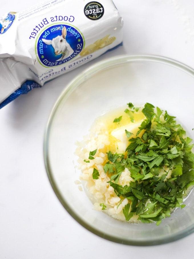 Ingredienti per burro all'aglio di latte di capra con ciotola di vetro con prezzemolo e aglio e sale su uno sfondo bianco, pronti per essere serviti su focaccia. 