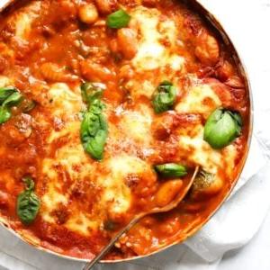 Gnocchi Facili al Forno 6 Una grande padella di Gnocchi al Forno cotti con mozzarella e basilico sopra, con un cucchiaio pronto per servire.