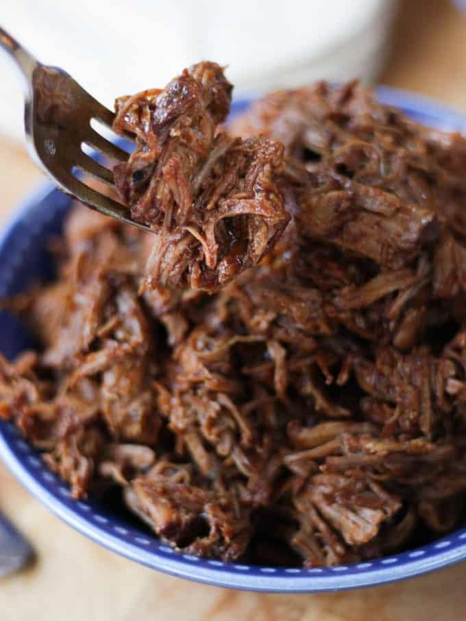 Maiale sfilacciato Instant Pot in una ciotola blu sollevato con una forchetta.