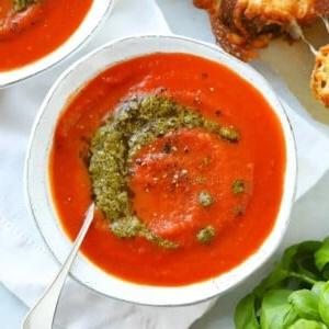 Facile Zuppa di Pomodoro {Ingredienti da dispensa} 6 Ricetta di zuppa di pomodoro facile con un ricciolo di pesto in una ciotola bianca.