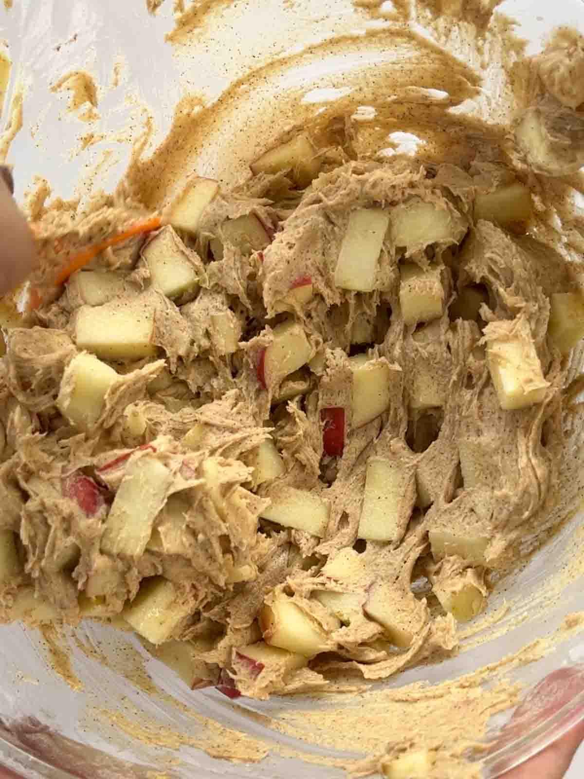 Torta di Mele Facile 6 Pezzetti di mela con impasto per torta in una ciotola di vetro.