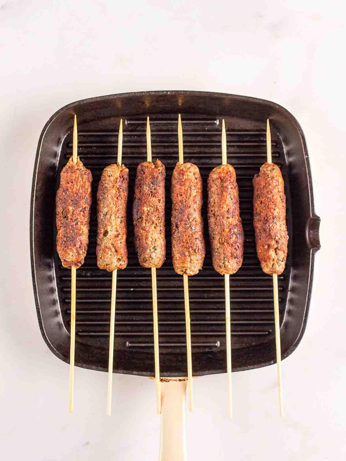 Facili Kofta di Agnello {con Tzatziki} 6 Kofta di agnello macinati con spiedini che cuociono su una piastra per il passaggio 3 del metodo di ricetta.