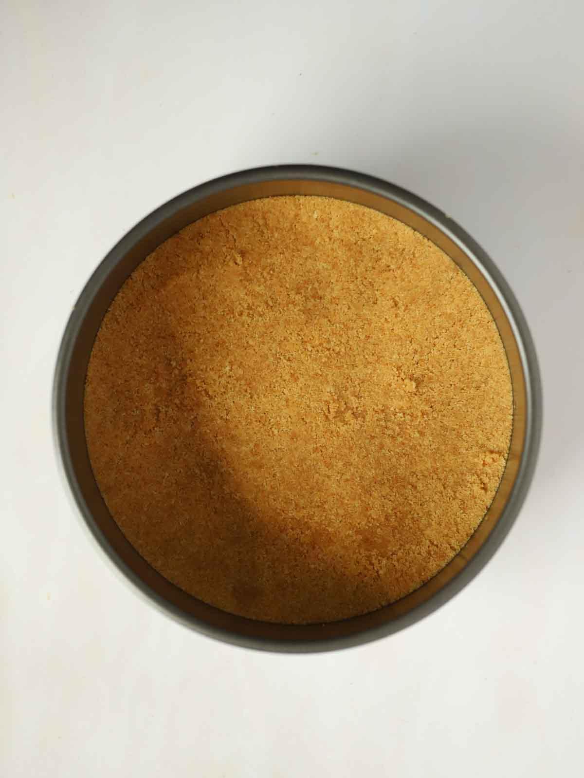 Una base di biscotti per una cheesecake alle fragole in una teglia, pronta per essere riempita.