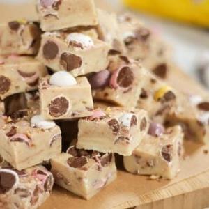 Una pila di quadrati di fudge al cioccolato bianco e mini uova su un tagliere.