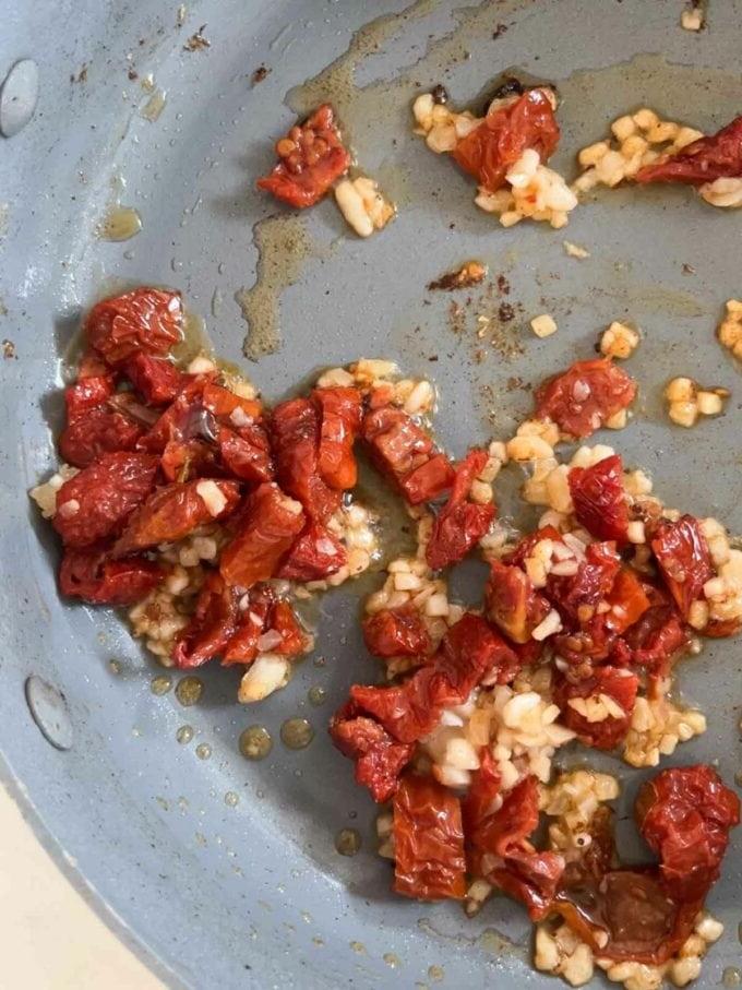 Aglio e pomodori secchi tritati cotti in olio in padella per la ricetta Pollo Sposami. Passaggio 3.