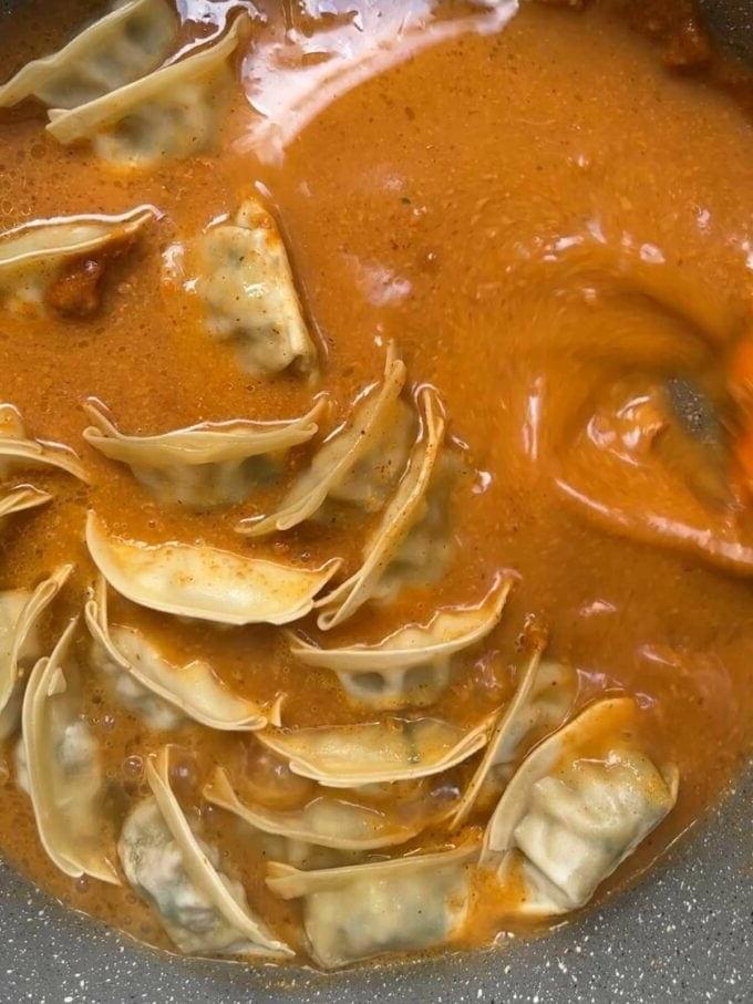Ravioli che cuociono in una casseruola per il passaggio 3 della ricetta della Zuppa di Gyoza.