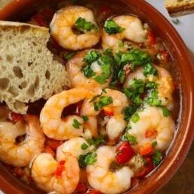 Un piatto di tapas spagnolo con gamberi ed erbe aromatiche e pane intinto per una facile ricetta di Gambas Pil Pil.