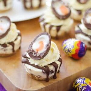 Mini Cheesecake Senza Cottura al Creme Egg 7 Mini Cheesecake alle Uova Crema di Pasqua con uovo crema tagliato sopra, su un tagliere di legno.