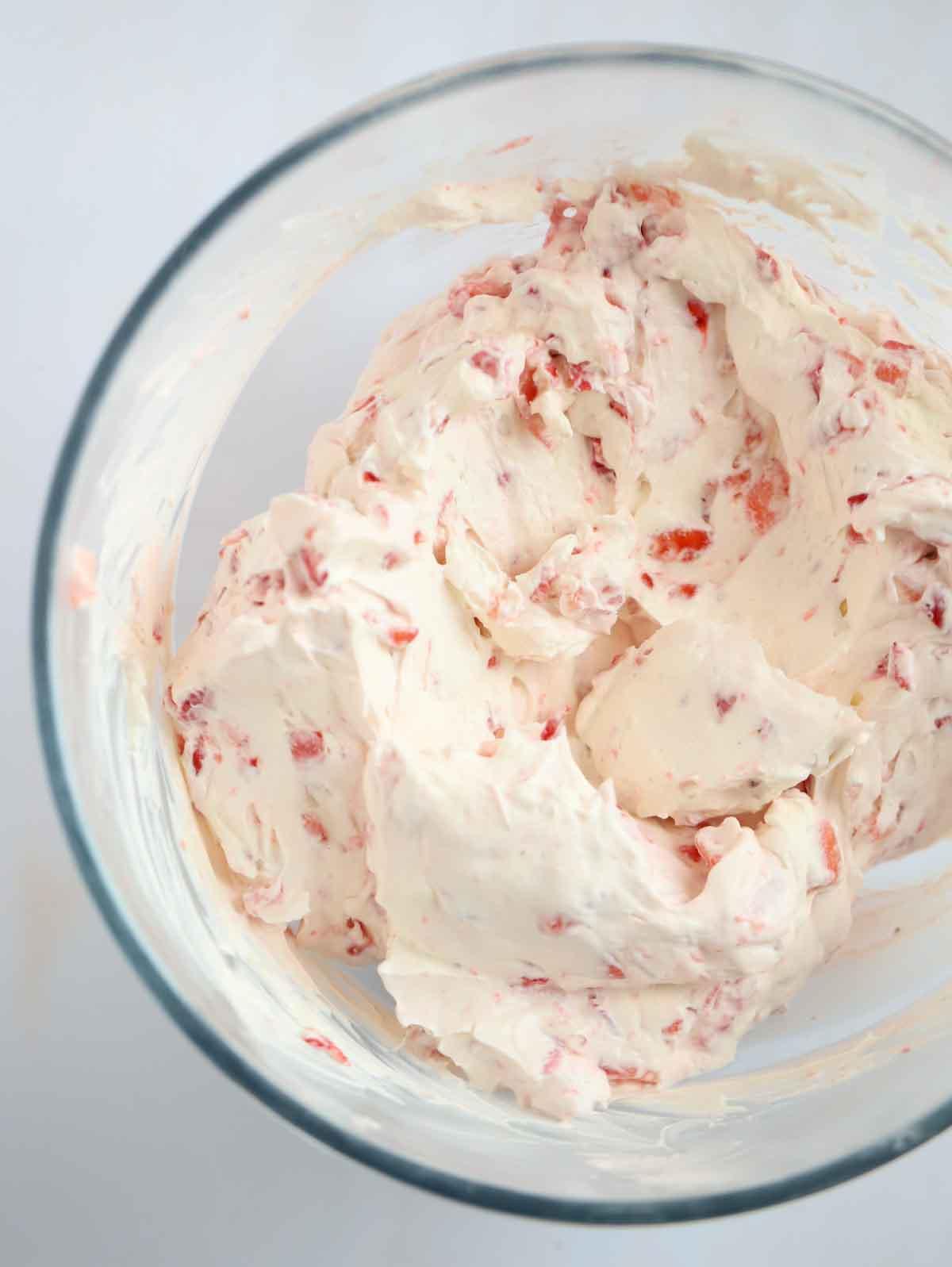 Panna montata e formaggio cremoso con fragole tritate in una ciotola per il passaggio 3 del processo di preparazione di una Cheesecake alle Fragole.