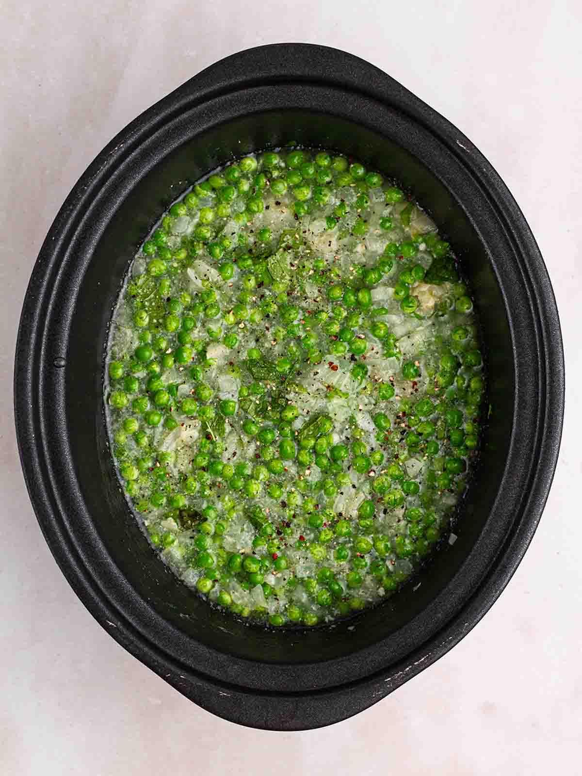 Una slow cooker con molti piselli per il passo 2 del processo per la Zuppa di Piselli e Prosciutto.