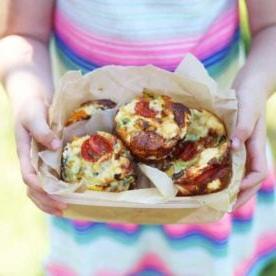 Un contenitore per il pranzo riempito con mini quiche senza crosta, tenuto nelle mani di una bambina.