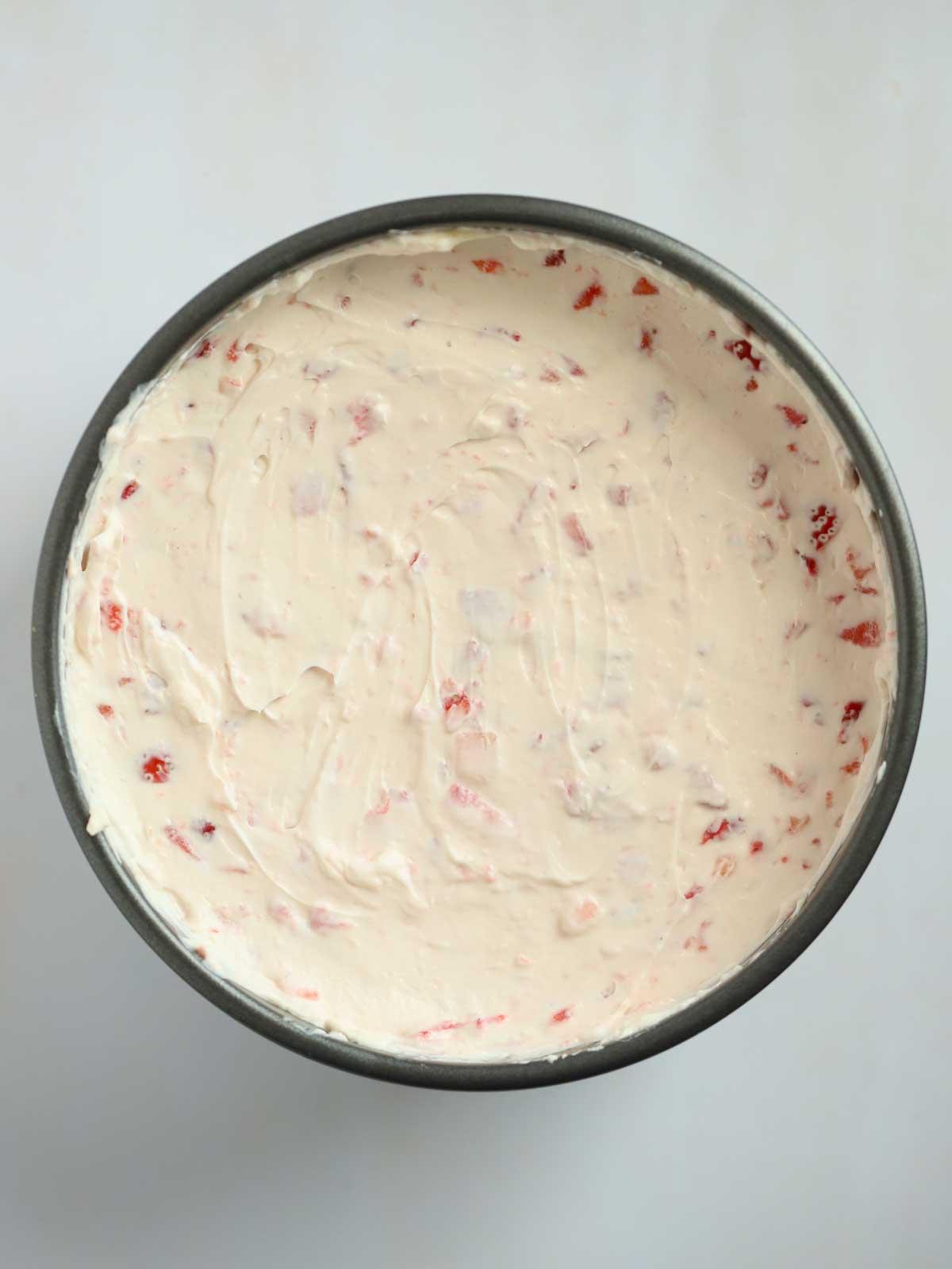 Una teglia riempita con crema e frutta per il passaggio 4 della ricetta della cheesecake alle fragole.