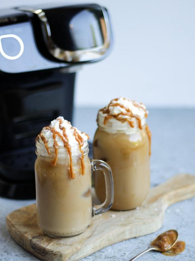Due tazze di vetro con manico di caffè freddo con caramello salato e capsule Tassimo sullo sfondo grigio con macchina da caffè Tassimo sullo sfondo.