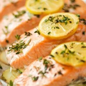 Una fila di salmone al forno con fette di limone ed erbe aromatiche sopra, appena sfornato.