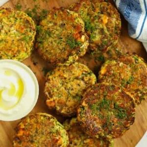 Frittelle di zucchine su un tagliere con una salsa cremosa.