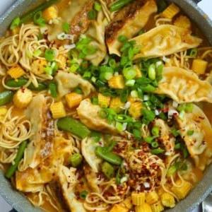 Una pentola piena di Zuppa di Gyoza abbondante, con noodles, ravioli e verdure in una salsa rossa thailandese.