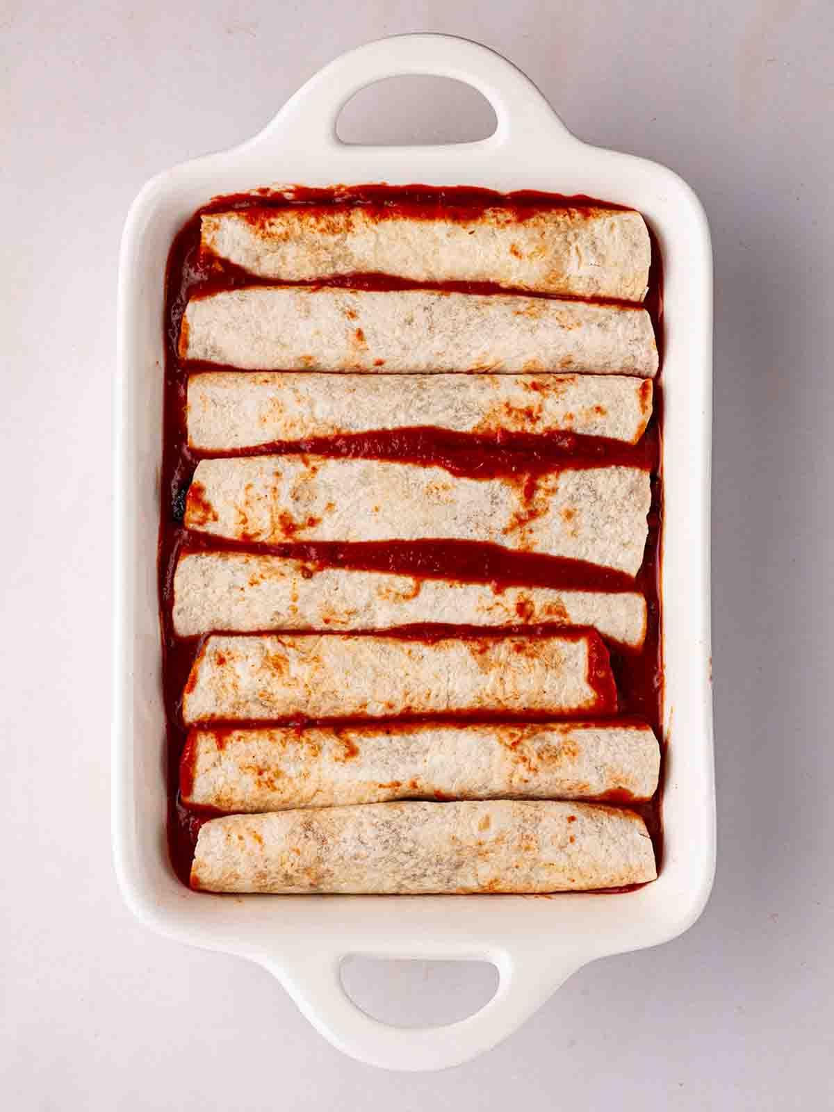 Enchiladas Vegetariane con Zucca Violina 9 Enchiladas Vegetariane arrotolate in una teglia bianca da forno per il passaggio 5 della ricetta delle Enchiladas Vegetariane.