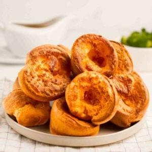 Yorkshire Puddings {Ricetta infallibile!} 9 Un mucchio di Pudding dello Yorkshire deliziosamente dorati su un piatto su un tavolo, pronti per essere serviti.