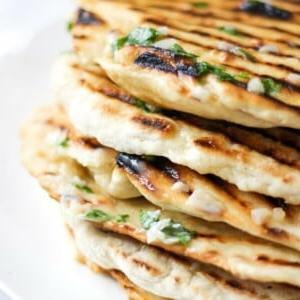 Focaccia Facile con Burro all'Aglio 9 Pila di focacce morbide facili da tre ingredienti con yogurt, con segni di griglia, burro all'aglio e prezzemolo su un piatto bianco.