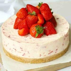 Un primo piano angolare di una cheesecake alle fragole, con la frutta abbondantemente disposta in cima.