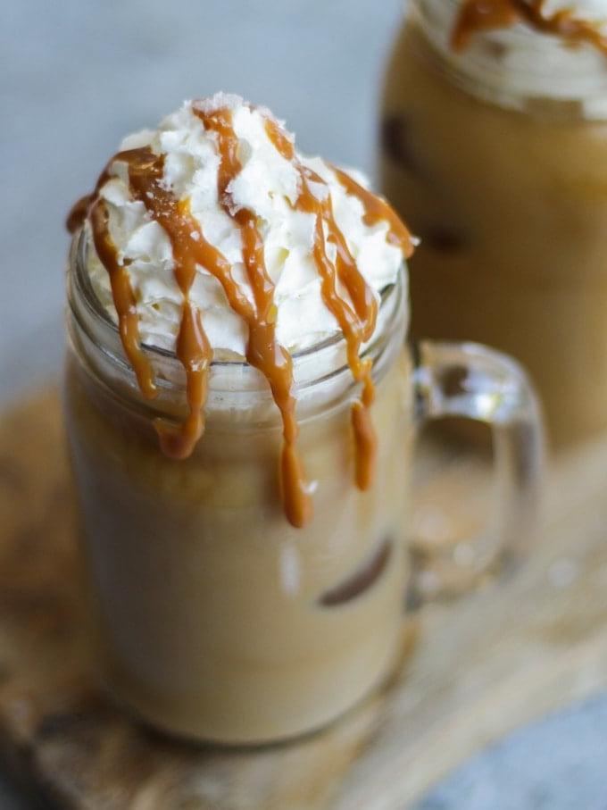 Una tazza di vetro con manico di caffè freddo, guarnita con panna montata e una colata di caramello salato.