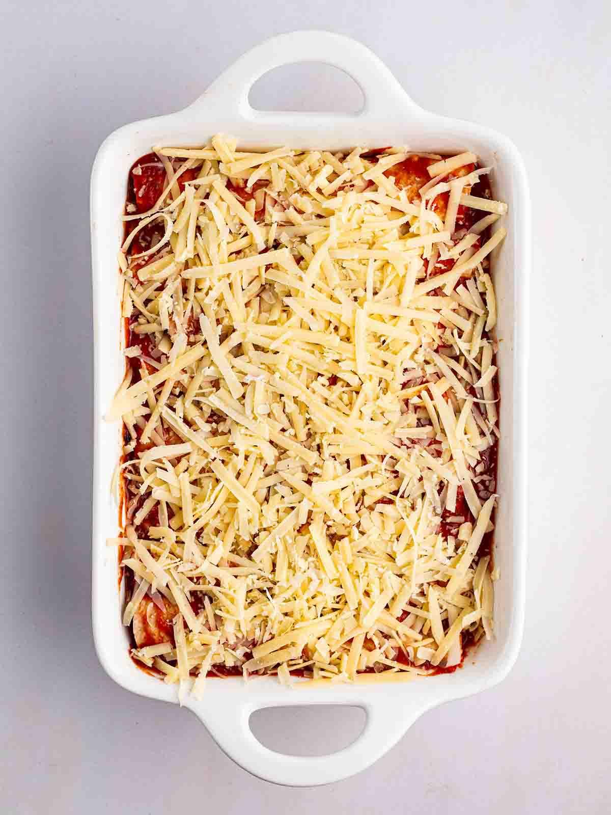 Enchiladas Vegetariane con Zucca Violina 10 Una teglia bianca da forno piena di enchiladas vegetariane e ricoperta di formaggio grattugiato per il passaggio 6 della ricetta delle Enchiladas Vegetariane.