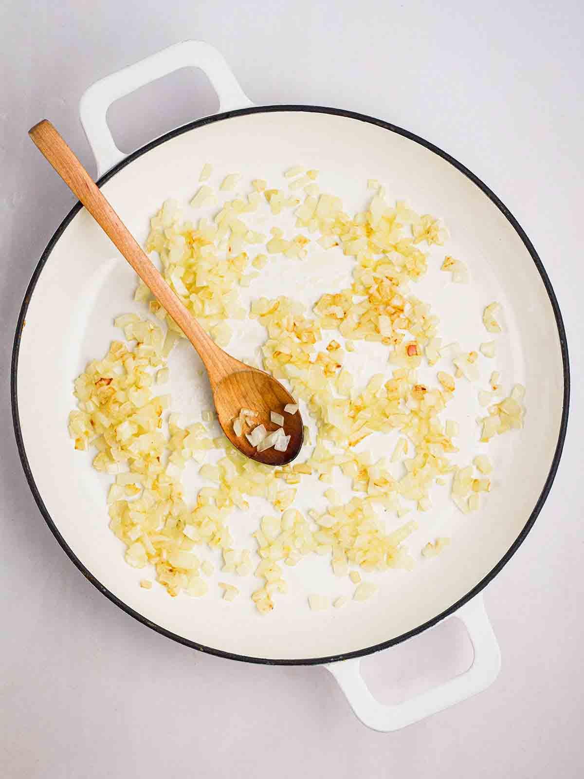 **Risotto di Zucca {Al Forno o Tradizionale}** 10 Una padella piena di cipolle che stanno dorando nell'olio e un cucchiaio di legno per mescolare.