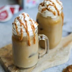 Due tazze di vetro con manico di caffè freddo con caramello salato e capsule Tassimo sullo sfondo grigio.
