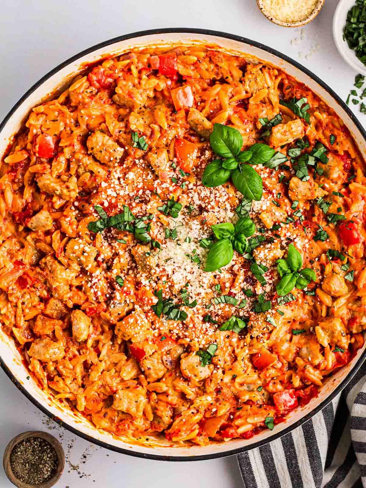 Semplice Orzo con Salsiccia {Pentola Unica} 2 Una grande pentola bianca su un piano di lavoro bianco riempita di Orzo con Salsiccia in una salsa al pomodoro e basilico fresco sopra.