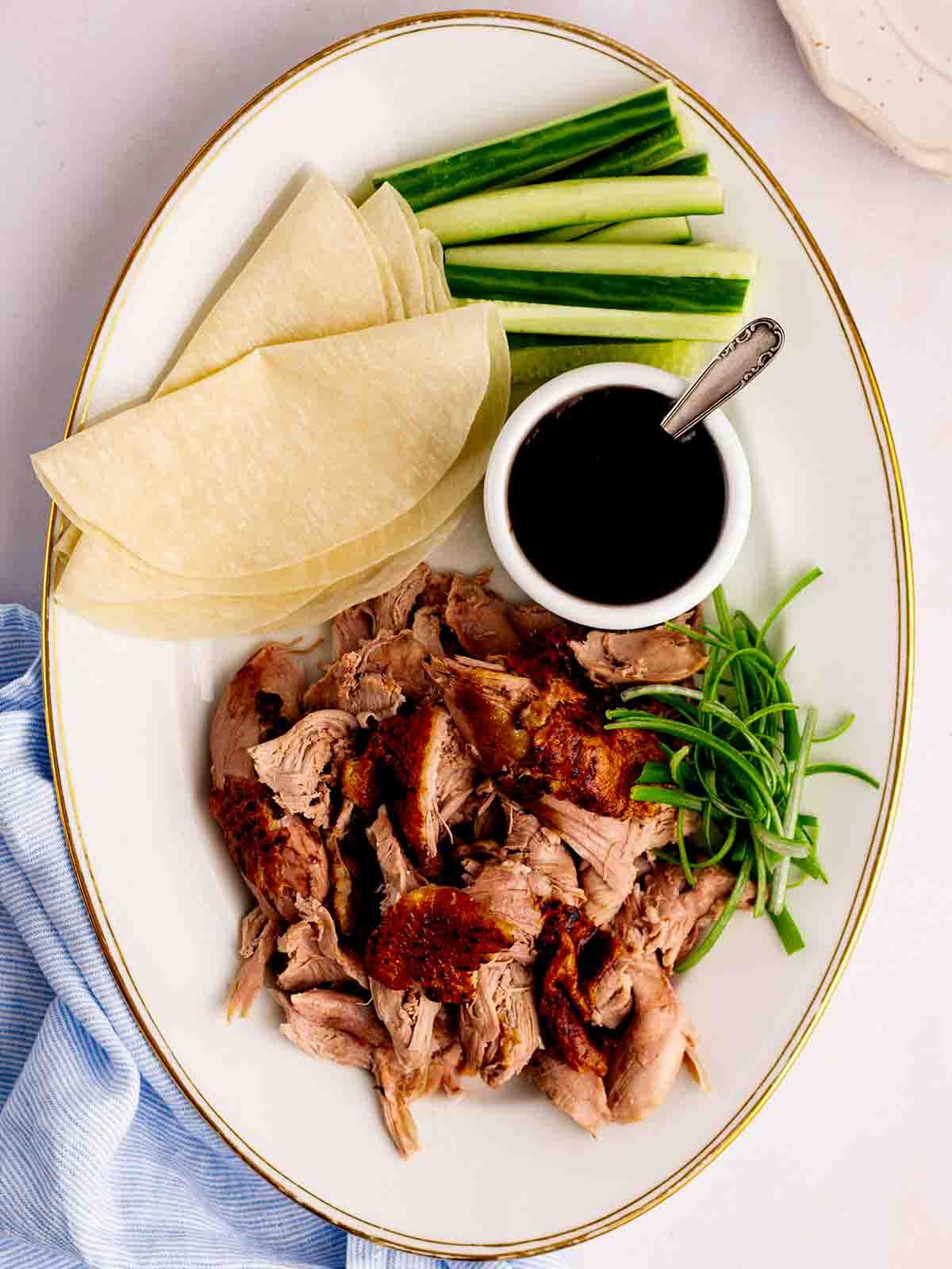 Anatra alla pechinese in pentola a cottura lenta 2 Un piatto con anatra cotta lentamente e sfilacciata, crepes cinesi, cetrioli, cipollotti e salsa.