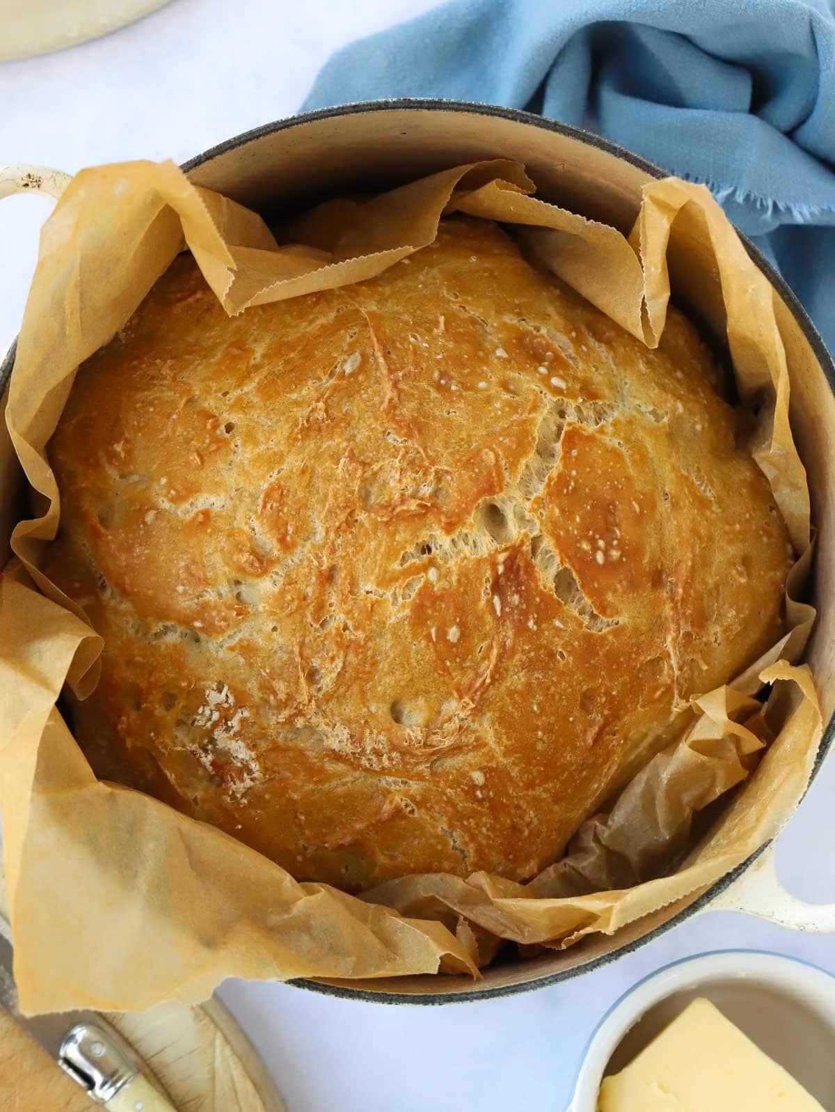 Pane Senza Impasto {La Ricetta Notturna Più Semplice di Sempre} 2 Una vista dall'alto di un filone di pane fatto in casa dorato in una pentola con carta da forno per la ricetta del Pane Senza Impasto.