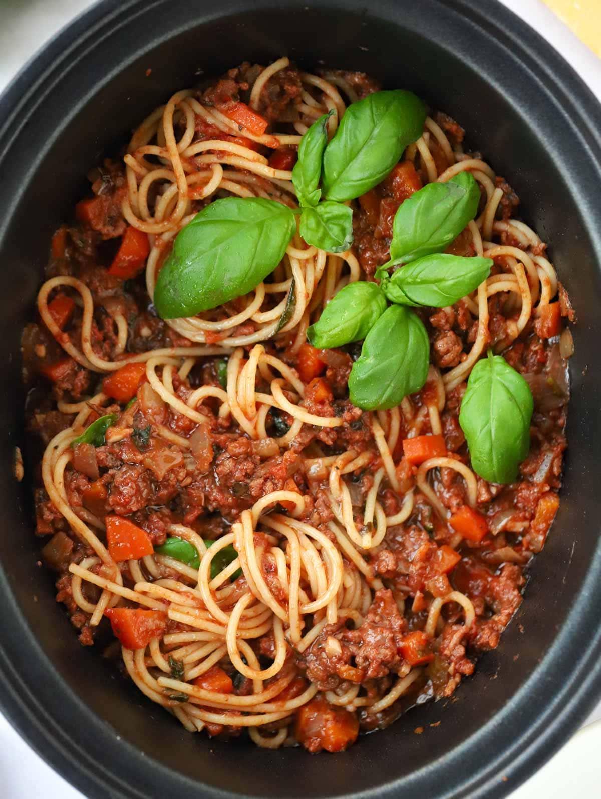 Bolognese a cottura lenta {Ricetta senza rosolatura!} 2 Salsa bolognese per slow cooker in una pentola slow cooker, mescolata con spaghetti cotti e guarnita con basilico.