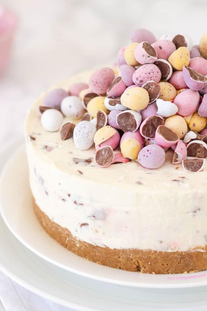 **Mini Cheesecake alle Uova** 2 Cheesecake guarnita con ovetti di cioccolato dai colori pastello su un piatto bianco.