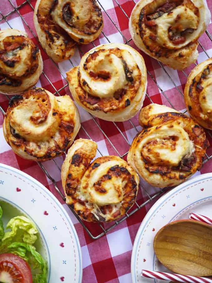 Rotolini di Pizza {Ricetta Facile!} 2 Una griglia su una tovaglia rossa e bianca con Girelle di Pizza appena sfornate, con un'insalata di contorno su un piatto.