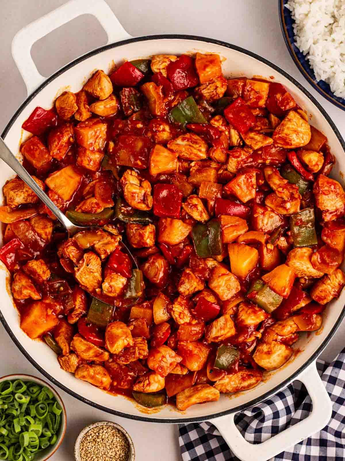 Pollo in Agrodolce {Ricetta Facile!} 2 Un padella bianca su un tavolo da pranzo piena di Pollo in Agrodolce cotto, pronto per essere servito.