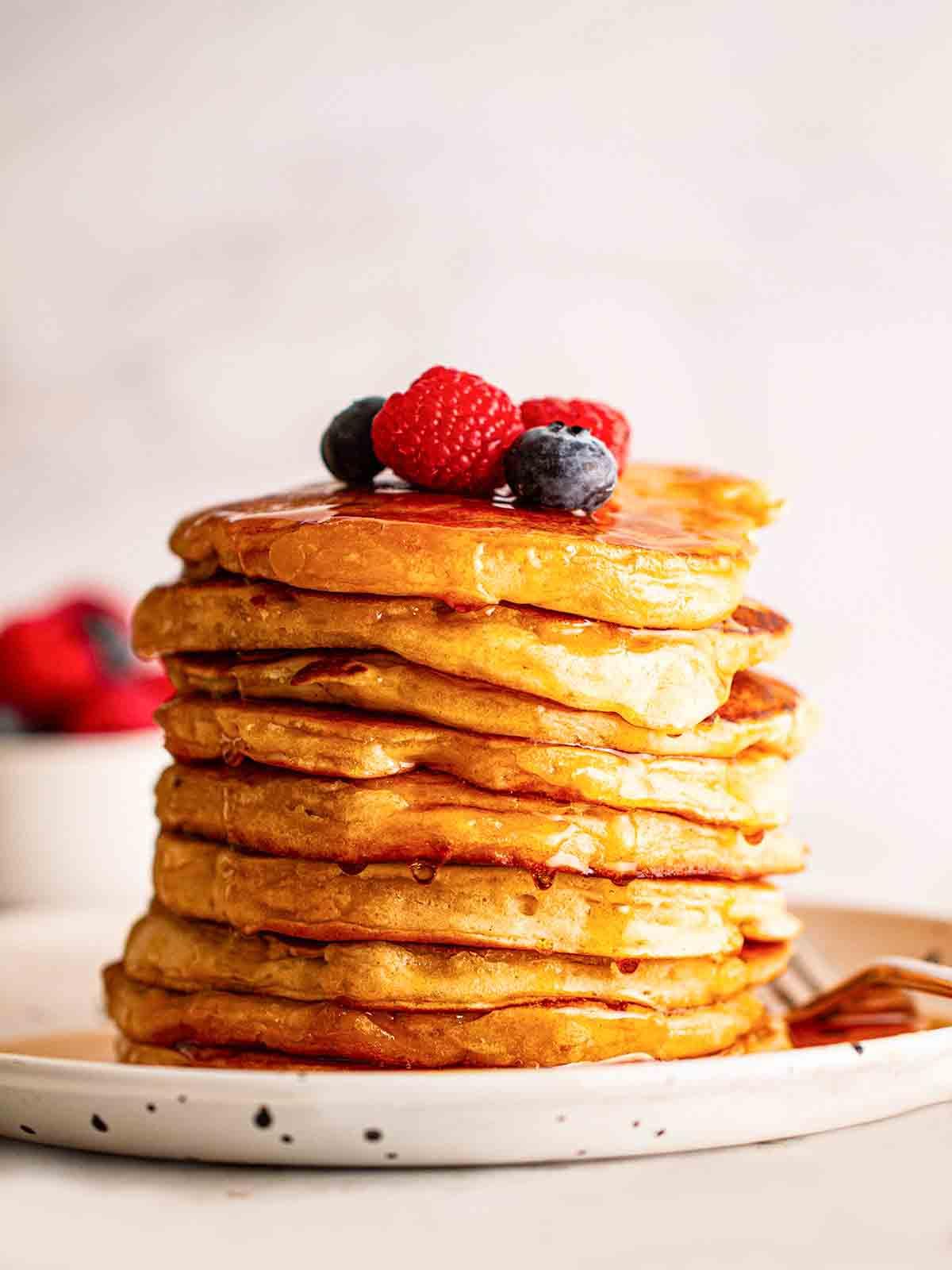 Pancakes Americani {Ricetta Facile!} 2 Un mucchio di soffici Pancakes Americani su un piatto con mirtilli e lamponi sopra.
