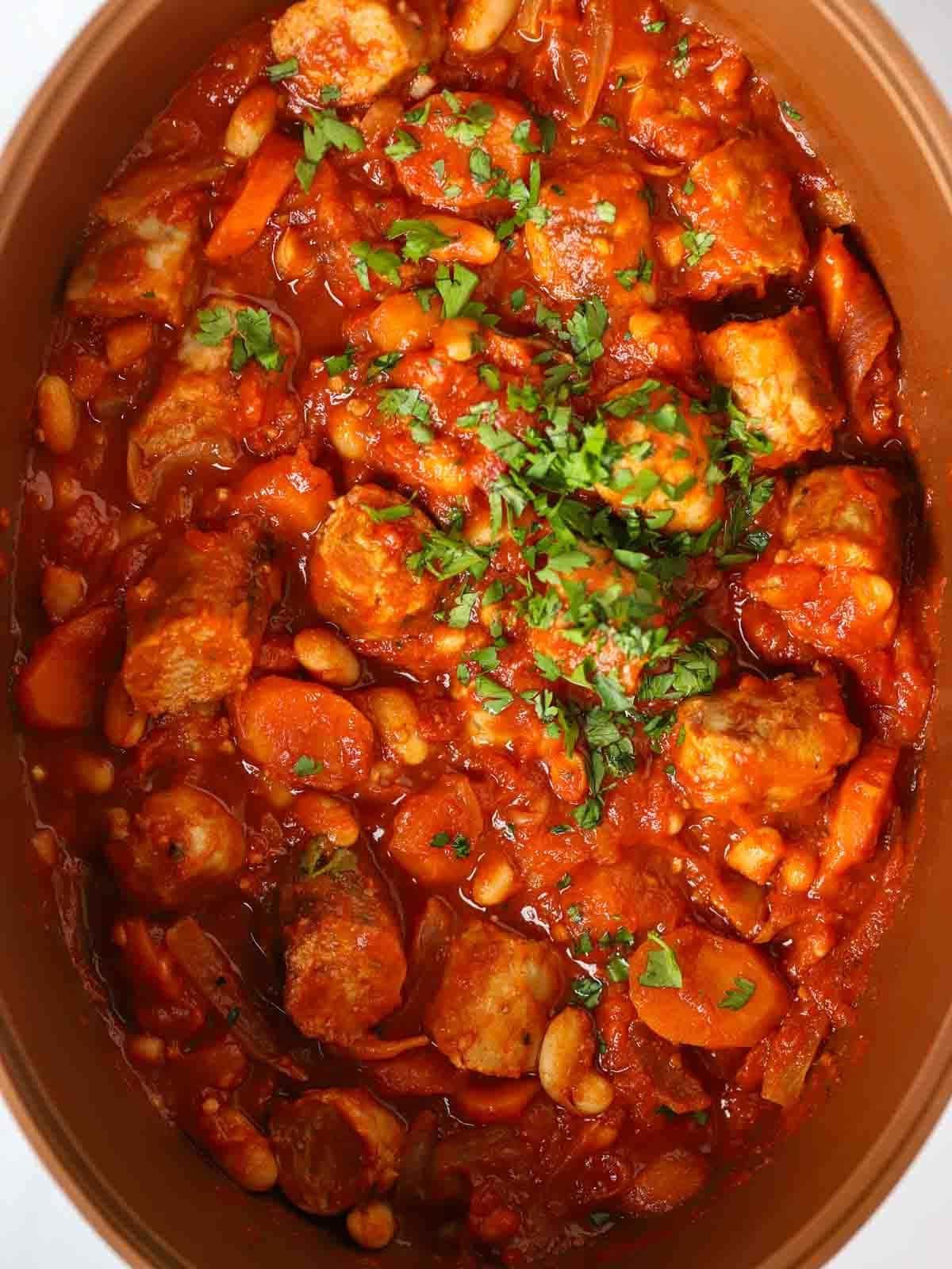 Stufato di Salsicce a Cottura Lenta {Ricetta Facile} 2 A slow cooker pan with a cooked sausage casserole inside, garnished with parsley.