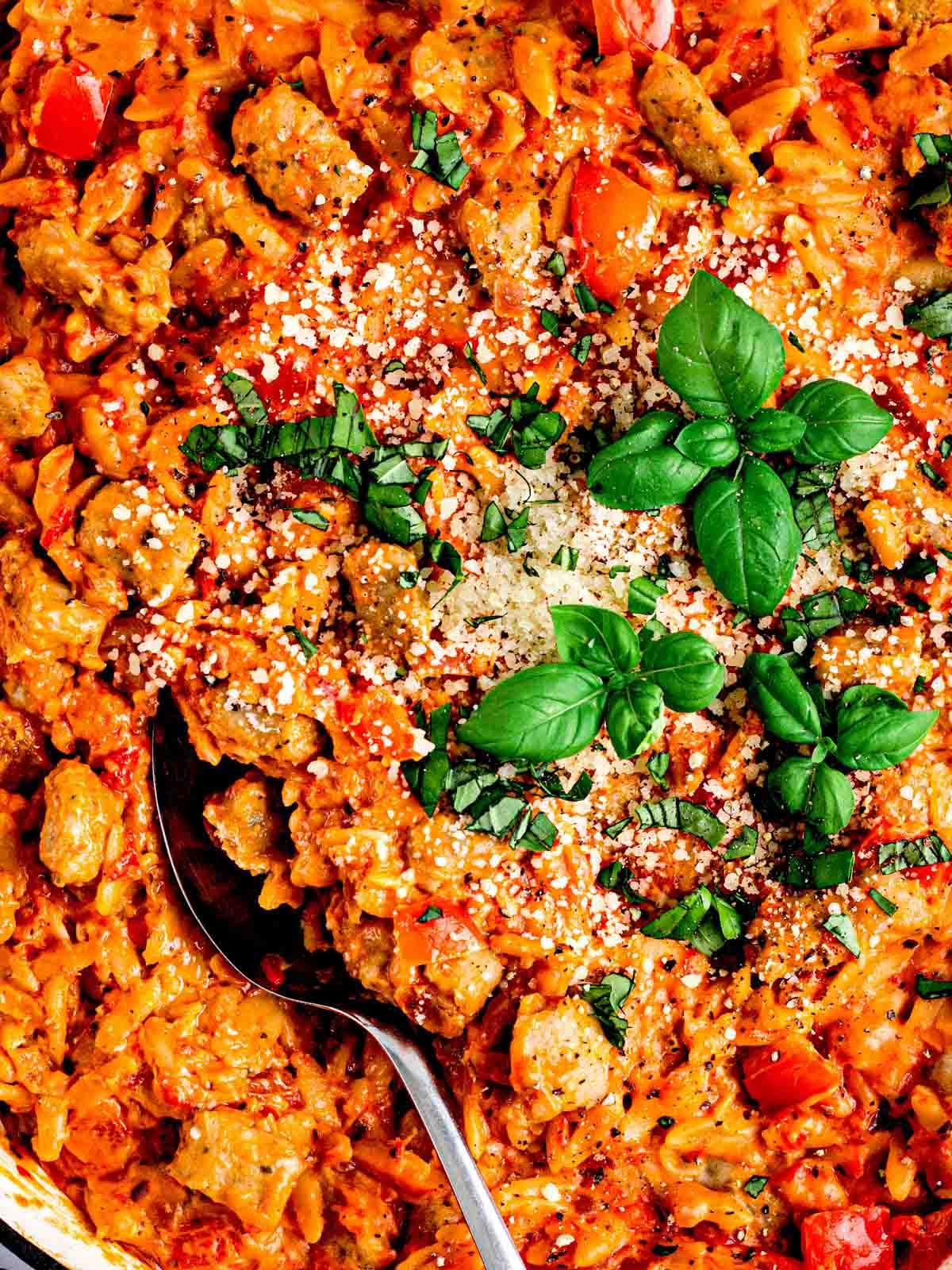 Semplice Orzo con Salsiccia {Pentola Unica} 3 Un primo piano di pasta Orzo con Salsiccia con un cucchiaio e basilico fresco sopra.