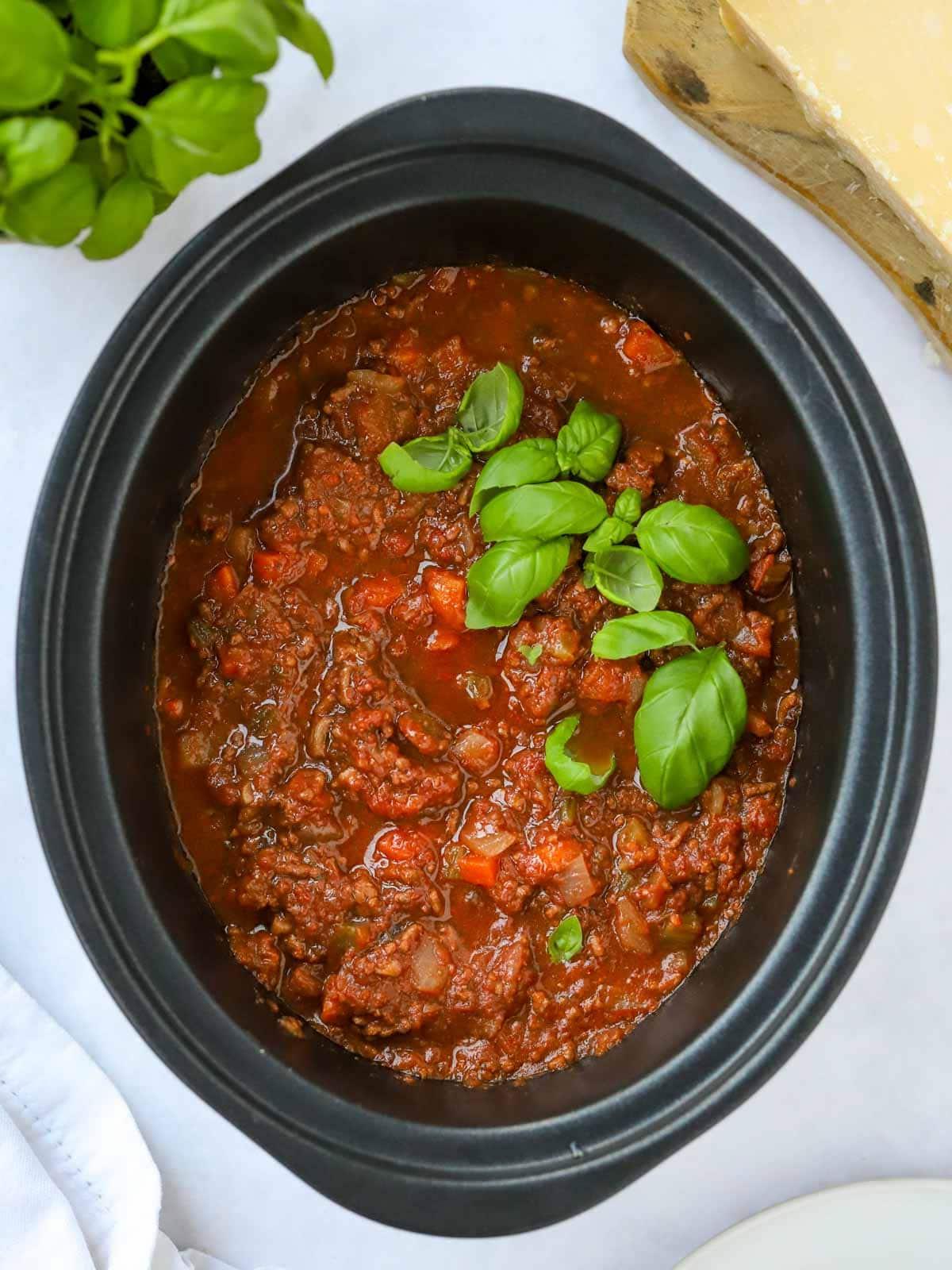 Bolognese a cottura lenta {Ricetta senza rosolatura!} 3 Ragù di manzo per slow cooker cotto in una pentola, con basilico sopra.