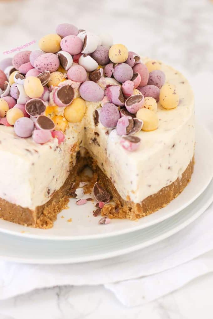 **Mini Cheesecake alle Uova** 3 Cheesecake ai Mini Egg con una fetta tagliata su due piatti bianchi sopra un tovagliolo.