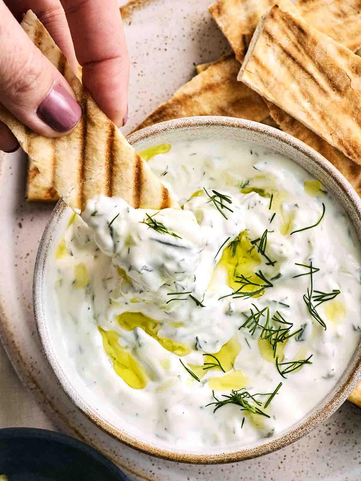 Tzatziki {Ricetta Facile!} 3 Una ciotola di Tzatziki con una pita che viene intinta.