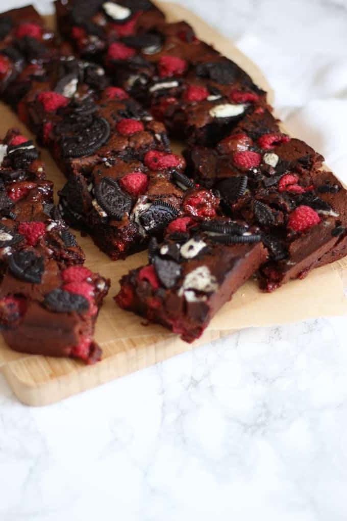 Angolo laterale di brownies Oreo gommosi con lamponi su un tagliere di legno su uno sfondo in marmo.