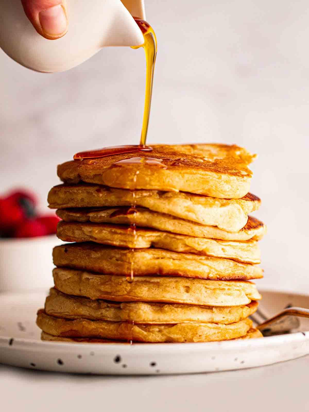Pancakes Americani {Ricetta Facile!} 3 Una grande pila di Pancakes Americani su un piatto con sciroppo d'acero che viene versato sopra da una caraffa.