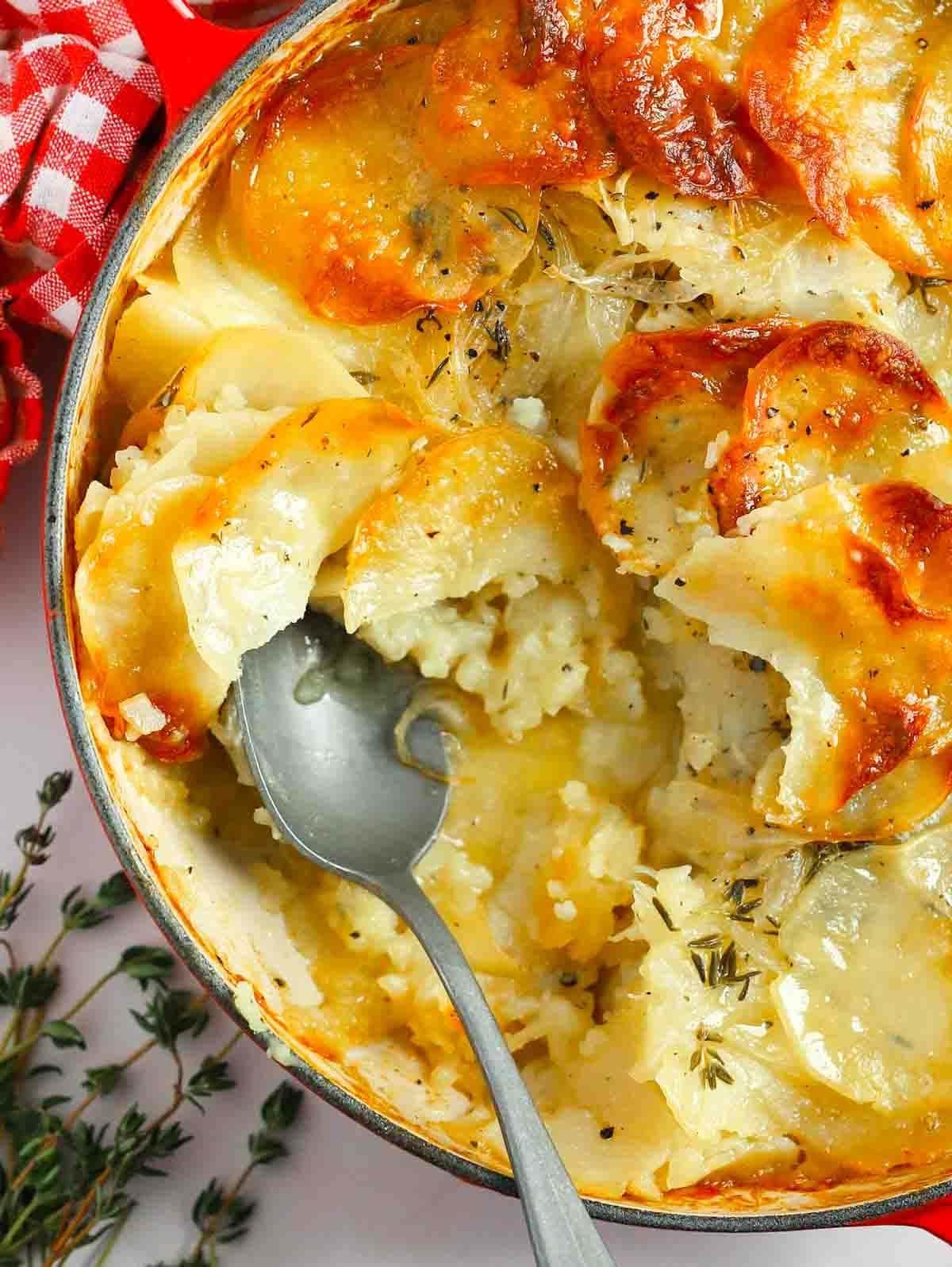 Patate alla Boulangère 3 Una teglia piena di Patate alla Boulangère cotte, con un cucchiaio e una porzione mancante.