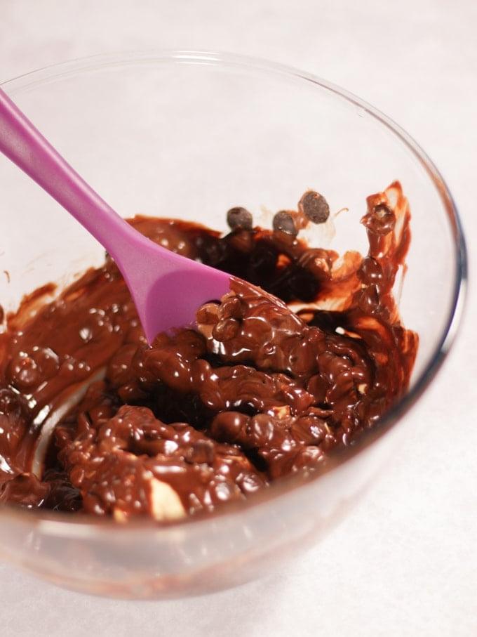 Ricetta Rocky Road al Creme Egg 3 Ciotola di vetro con ingredienti per il Rocky Road con Creme Egg (cioccolato, burro e sciroppo dorato) con un cucchiaio viola.