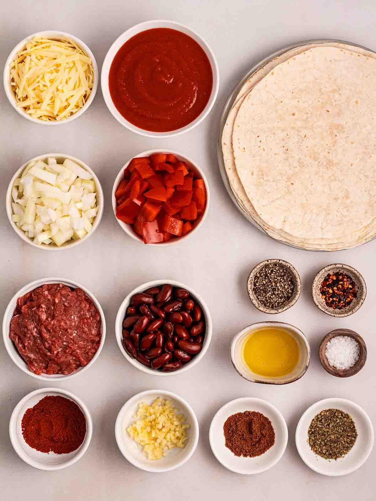 Enchiladas di Manzo 4 Gli ingredienti per preparare le Enchiladas di Manzo disposti in ciotole e piatti su una superficie bianca.
