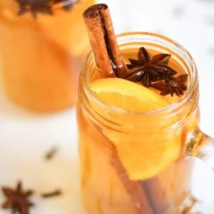 Sidro Caldo Speziato {Ricetta Facile per Slow Cooker} 4 Primo piano di un barattolo di vetro di sidro caldo speziato, guarnito con bastoncino di cannella, anice stellato e una fetta d'arancia.