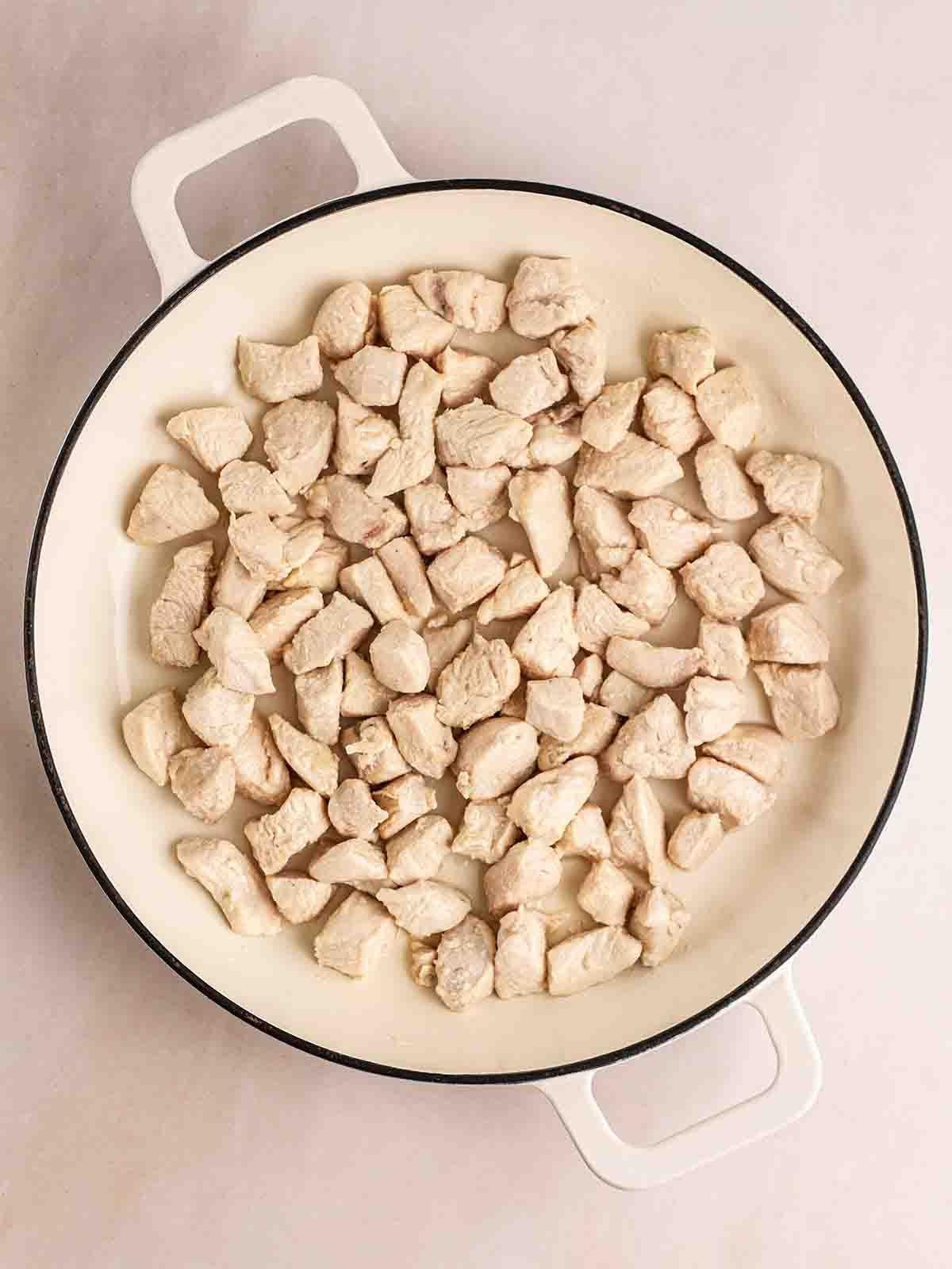 Pollo in Agrodolce {Ricetta Facile!} 4 Una padella bianca piena di pezzi di petto di pollo a cubetti cotti, per il passaggio 1 della ricetta del Pollo in Agrodolce.
